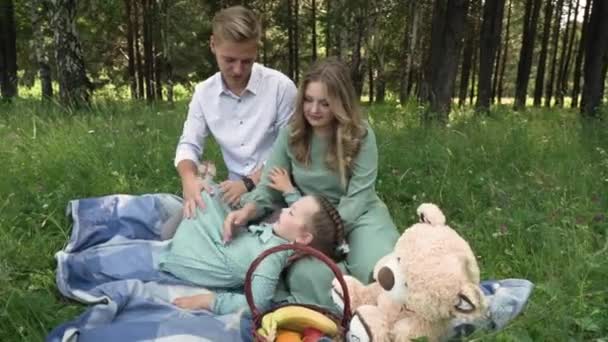 Padre, madre e figlioletta sono seduti su una coperta all'ombra degli alberi nella foresta — Video Stock