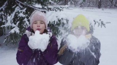 İki genç kız karda diz çöküp kar topu atarak eğleniyorlar. Kış eğlencesi