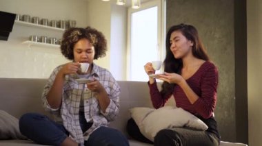 İki Afro-Amerikalı ve Asyalı kız arkadaş evde çay içerken gülüyorlar.