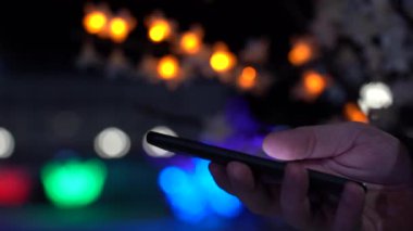 Akıllı telefonu tutan ellerin yakın çekimi. Arka planda şehir ışıkları
