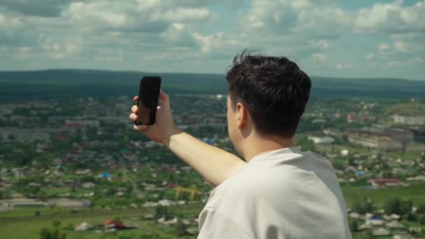 一个年轻的成年男子在一座大山顶上拍了一张智能手机的照片. — 图库视频影像