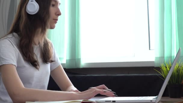 Kulaklık takan kız öğrenci internet öğretmeniyle çalışıyor, dizüstü bilgisayara bakıyor. — Stok video