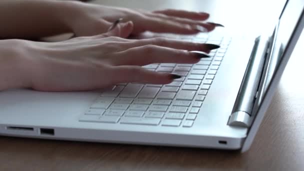 Mãos femininas de uma mulher digitando em um teclado de laptop enquanto sentada em sua mesa — Vídeo de Stock