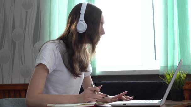 Dziewczyna student noszenia słuchawek studiuje online z nauczycielem Internetu, patrząc na laptopa — Wideo stockowe
