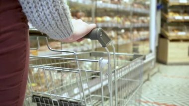 Genç bir bayan müşterinin eli boş bir el arabasını süpermarketin koridorlarında taşıyor.
