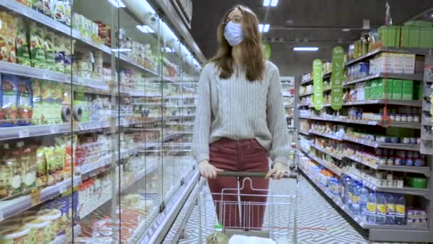 Großaufnahme einer jungen Frau, die einen Einkaufswagen durch die Gänge eines Supermarktes bewegt, das Konzept von Verkauf und Einkauf — Stockvideo