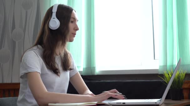 Meisje met een koptelefoon die online studeert met een internetleraar, op zoek naar een laptop — Stockvideo