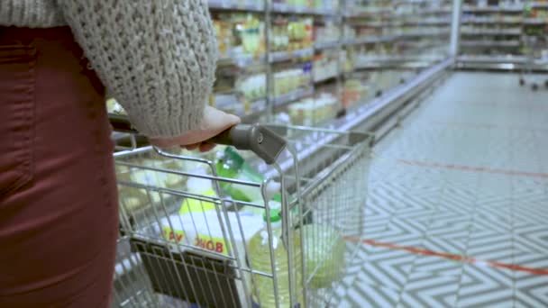 Крупним планом молоді жіночі руки переміщують продуктовий візок через проходи супермаркету, концепцію продажу і покупки — стокове відео