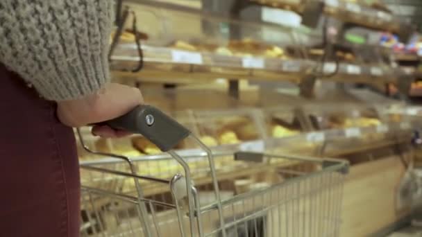 Primer plano de un joven manos de mujer moviendo un carrito de comestibles a través de los pasillos de un supermercado, el concepto de venta y compras — Vídeos de Stock