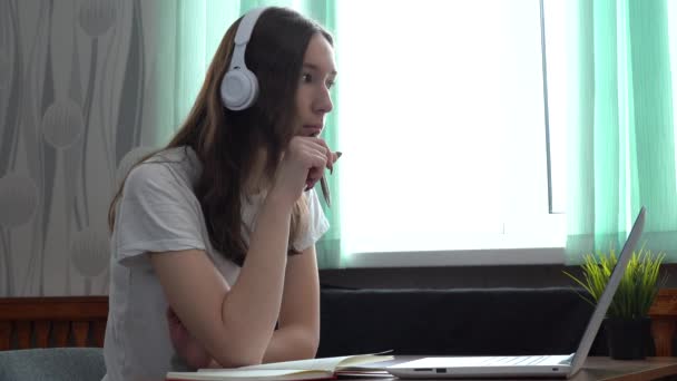 Étudiante portant un casque étudiant en ligne avec un professeur d'Internet, regardant un ordinateur portable — Video