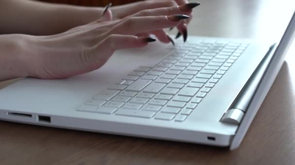 Manos femeninas de una mujer escribiendo en un teclado portátil mientras está sentada en su escritorio — Vídeo de stock