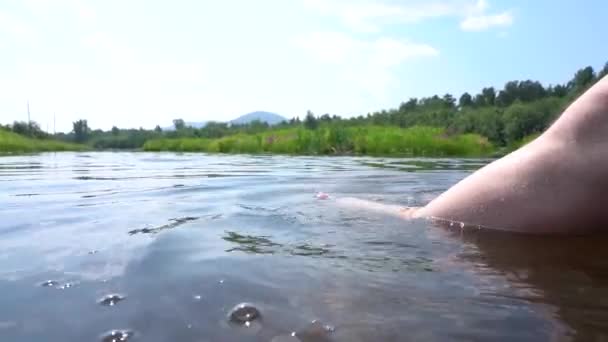 Muž si užívá letní prázdniny tím, že sedí na dřevěné desce s nohama v říčce — Stock video