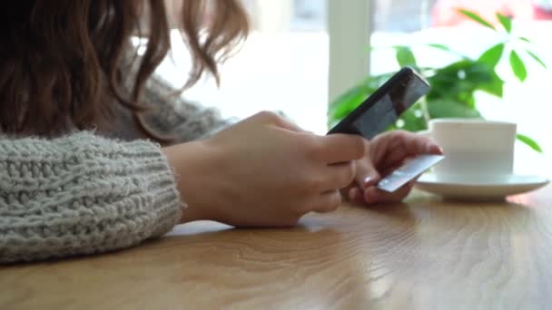 Bir kafede otururken elinde akıllı telefon ve kredi kartı planı tutan bir kız. — Stok video