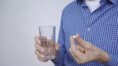 Bir bardak su ve beyaz yuvarlak hap tutan bir adamın elleri.