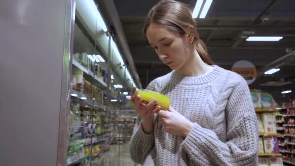 Een jonge vrouwelijke klant leest de samenstelling van de drank op de sapfles — Stockvideo