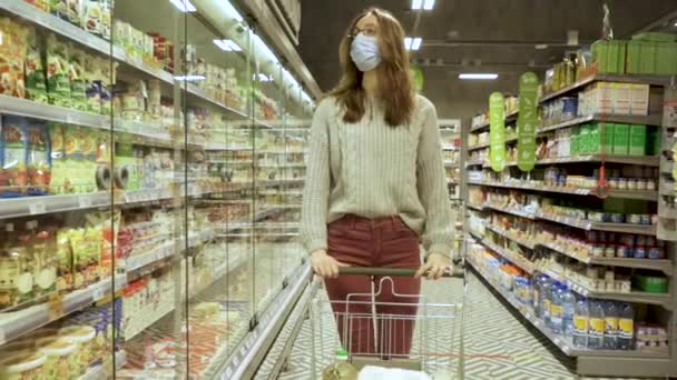 Gros plan d'une jeune femme qui déplace un chariot d'épicerie dans les allées d'un supermarché, concept de vente et de magasinage — Video