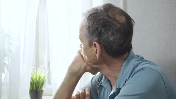 Tylny widok starszego mężczyzny, samotnego, wyglądającego przez okno, siedzącego w domu i wspominającego przeszłość — Wideo stockowe