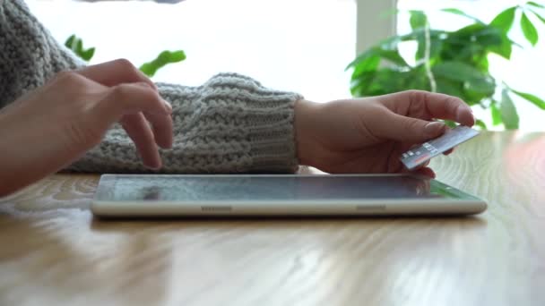 Une fille tient une carte de crédit et utilise une tablette alors qu'elle est assise dans un café pour faire un achat — Video