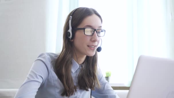 Egy fiatal nő fejhallgatót visel, online kommunikál laptopon keresztül, magyarázza, tanítja. Távolsági oktatás, üzletasszony tanácsadás ügyfél — Stock videók