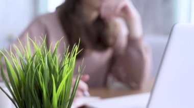 Ön plandaki saksıdaki bitki. Genç bayan öğrenci not defterine yazar ya da çizer.