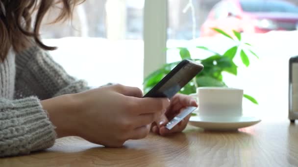 Mädchen hält Smartphone und Kreditkarte in der Hand, während sie im Café sitzt — Stockvideo