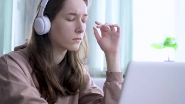 Evde ders çalışan, nezle olmuş, burnunu silen liseli kız. Kulaklık takan kız öğrenci internet öğretmeniyle çalışıyor, dizüstü bilgisayara bakıyor.