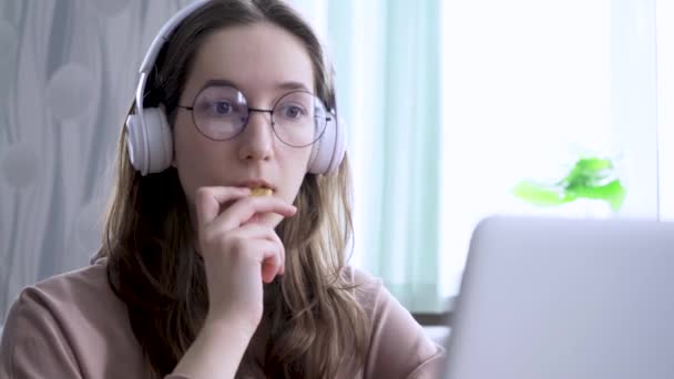 Evde bir kız çevrimiçi yayın izliyor ve kurabiye kemiriyor. — Stok video