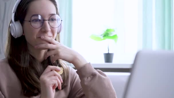 Tini lány laptoppal eszik cookie-kat, miközben filmet néz. — Stock videók