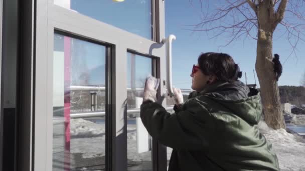 Uma jovem mulher feliz limpa diligentemente a porta de vidro — Vídeo de Stock