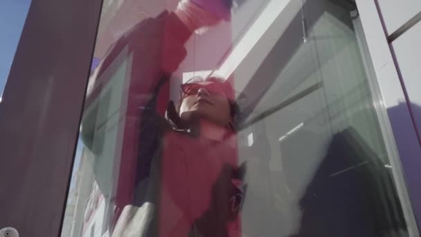 Eine fröhliche junge Frau putzt fleißig die Glastür — Stockvideo
