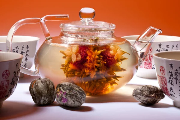 A glass teapot with a Chinese Floral Jasmain Tea Bulb which opens to reveal a flower when hot water is added. Three other floral bulbs are in the foreground.