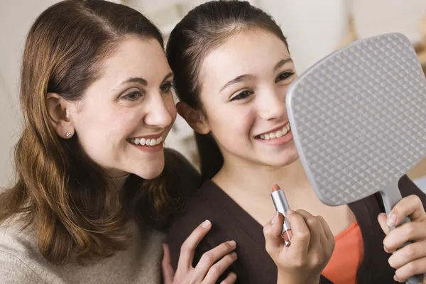 Lachende moeder en dochter met lippenstift, spiegel kijken Stockfoto