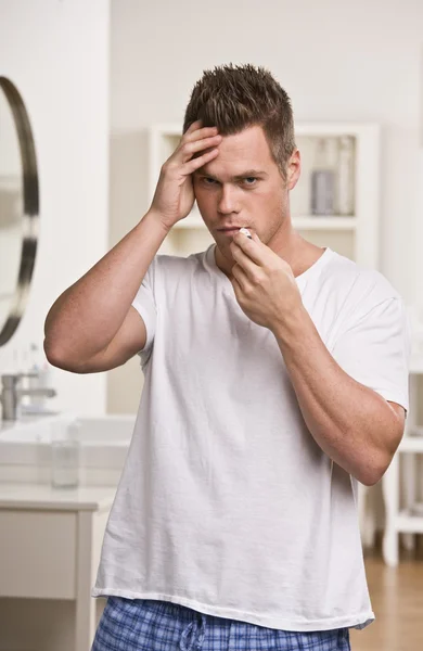 Man håller huvudet och ta temperaturen — Stockfoto