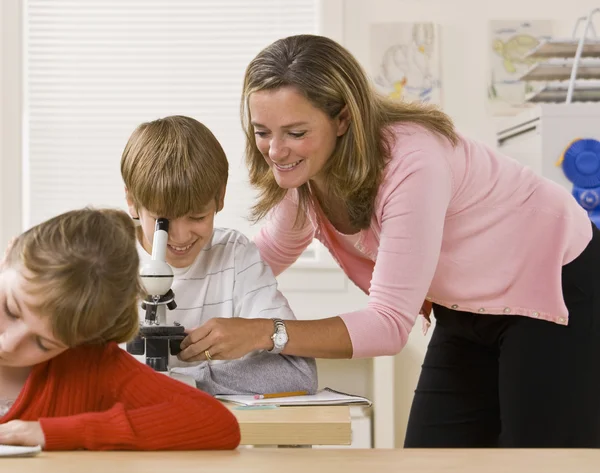 Profesor ayudando a estudiante con microscopio — Foto de Stock