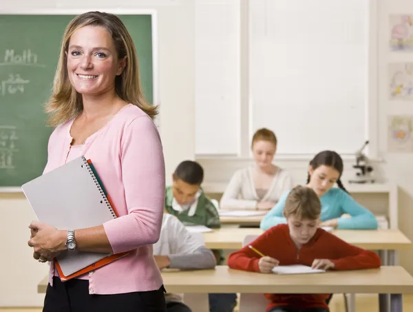 Lehrer steht mit Notizbuch im Klassenzimmer lizenzfreie Stockbilder