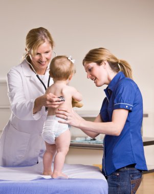 Doktor, bebeğe doktor muayenehanesinde check-up yapıyor.