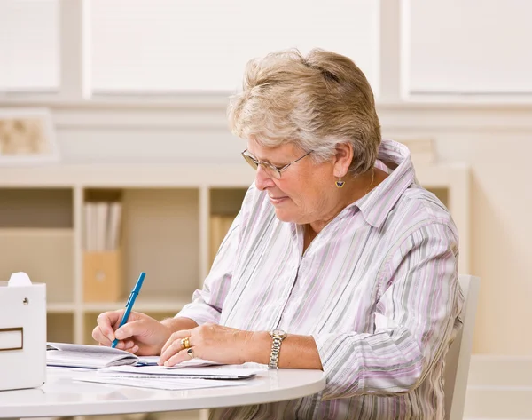 Senior vrouw controles schrijven — Stockfoto