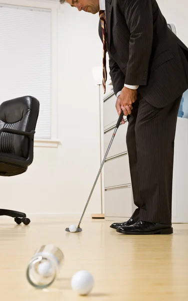 Empresario poniendo pelota de golf en la oficina —  Fotos de Stock