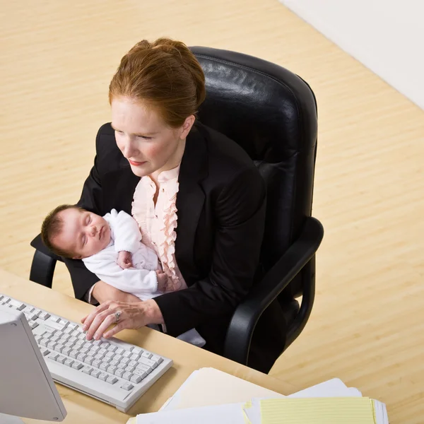 Donna d'affari che tiene il bambino alla scrivania — Foto Stock