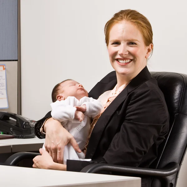 Businesswoman holding baby at desk — Stock Photo, Image