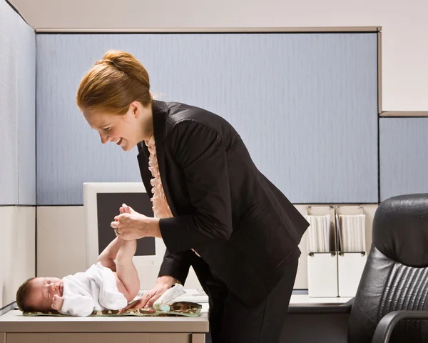 Businesswoman changing baby diaper at desk — Stock Photo, Image