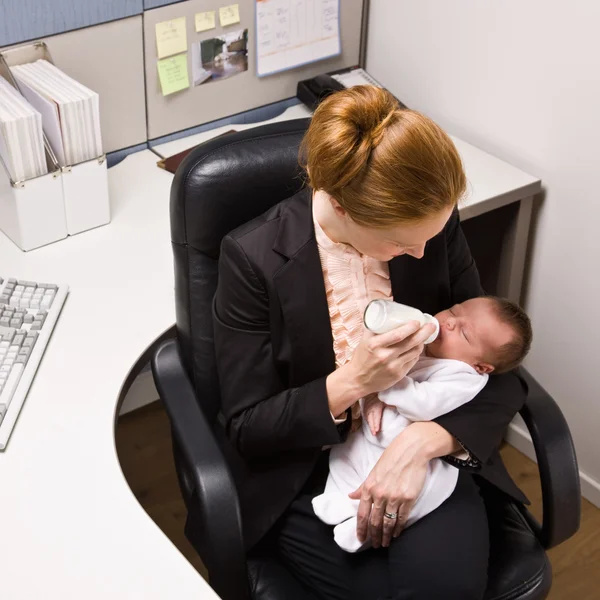 Affärskvinna utfodring baby på skrivbord — Stockfoto