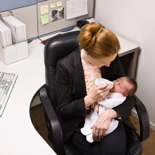 Donna d'affari che alimenta il bambino alla scrivania — Foto Stock