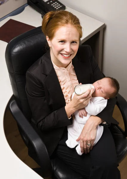 Businesswoman feeding baby at desk — Stock Photo, Image