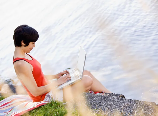 Woman using laptop near pond — Stock Photo, Image