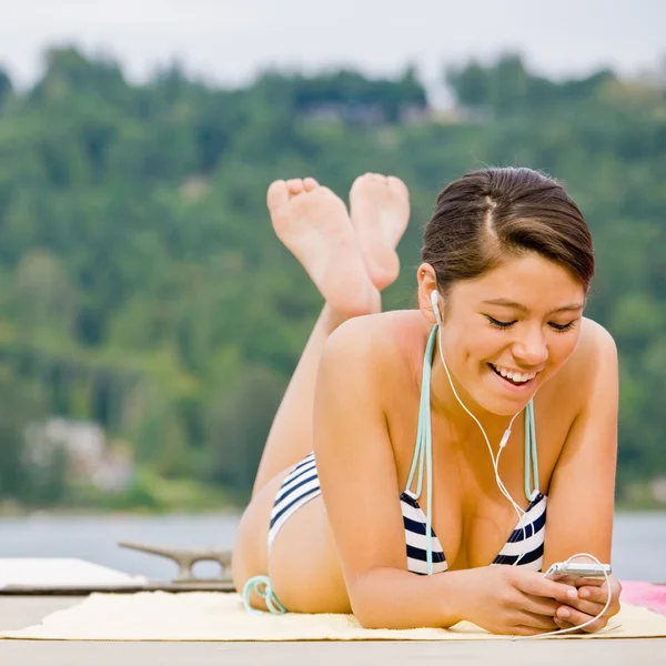 Woman laying on pier listening to mp3 player — Stock Photo, Image
