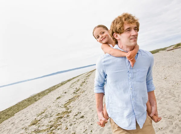 Fadern ger dotter piggy tillbaka rida på stranden — Stockfoto