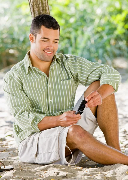 Man van het tekstoverseinen op mobiele telefoon op strand — Stockfoto