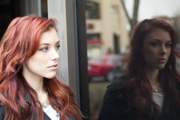 Молодая женщина с красивыми рыжими волосами, отражёнными в окне — стоковое фото