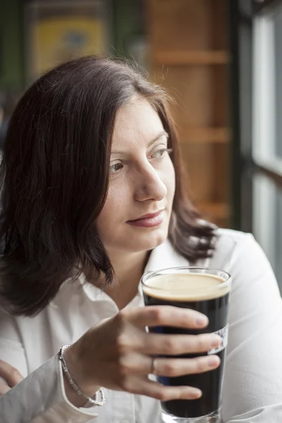 Mulher jovem com belos olhos castanhos bebendo uma caneca de Stout — Fotografia de Stock